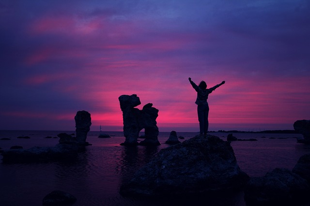 Someone stood on a rock in the sea with arms outstretched