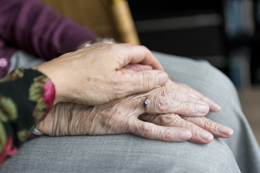 Aged hands on lap with younger hand on top.